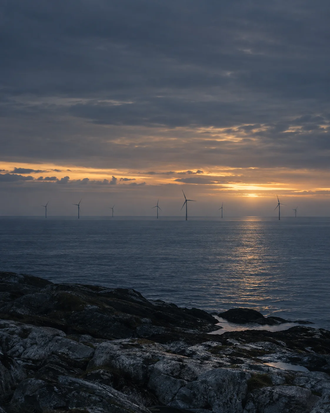Illustrative offshore wind turbines at sunset, representing investment in physical energy infrastructure.