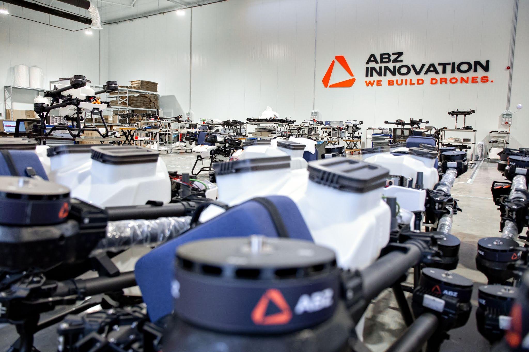 Rows of civilian multirotor drones on the floor of an ABZ Innovation factory, with the company name on the far wall.